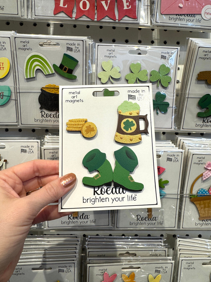 Load image into Gallery viewer, Hand holding a package of decorative magnets with shamrock design in a store setting.
