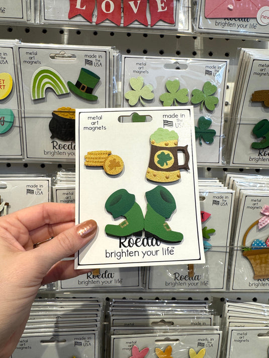 Hand holding a package of decorative magnets with shamrock design in a store setting.